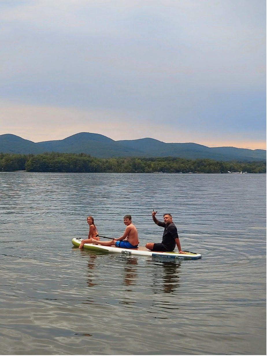 Family of three relaxing on a paddleboard on a Berkshire lake at sunset with Mt. Greylock in the background